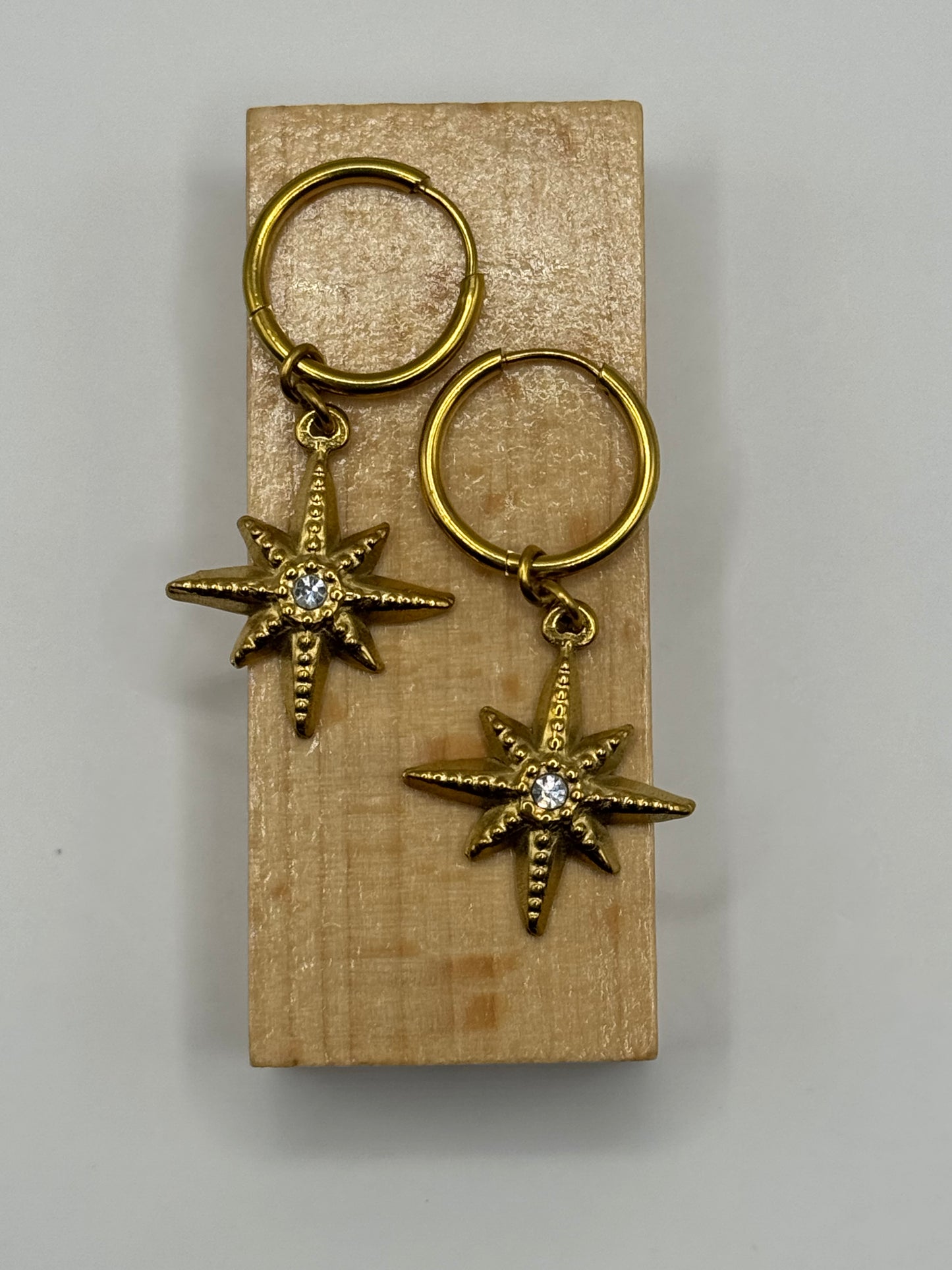 Flat lay of The Meridian Star gold huggie earrings with star charm and cubic zirconia center.