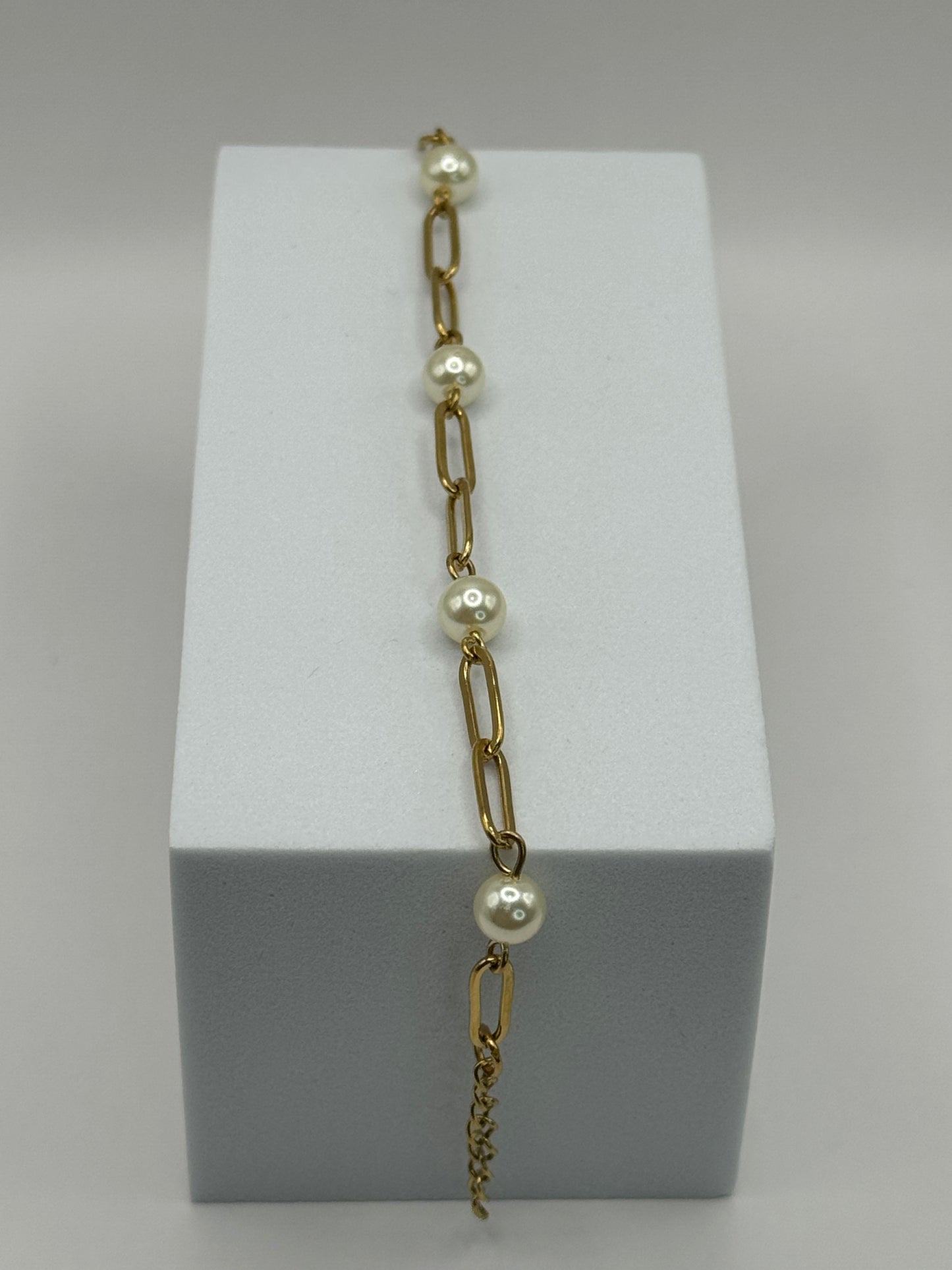 Gold paperclip chain bracelet with pearl stations displayed vertically on a white jewelry block.