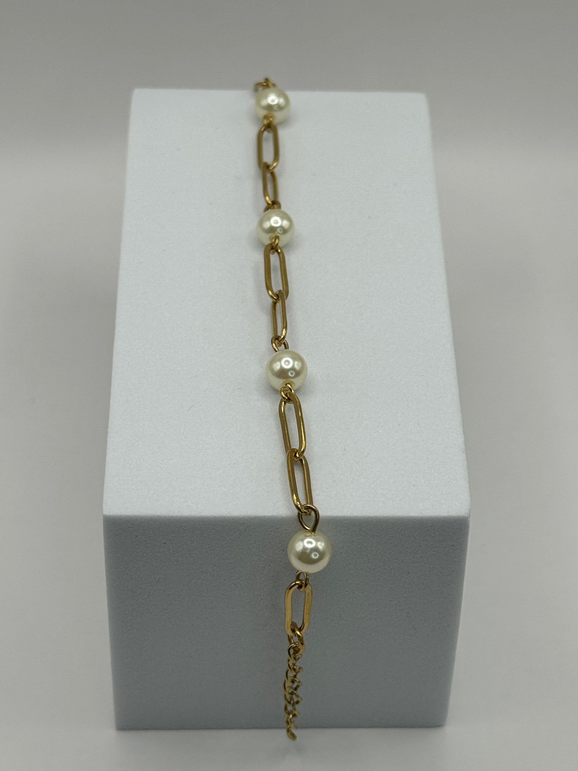 Gold paperclip chain bracelet with pearl stations displayed vertically on a white jewelry block.