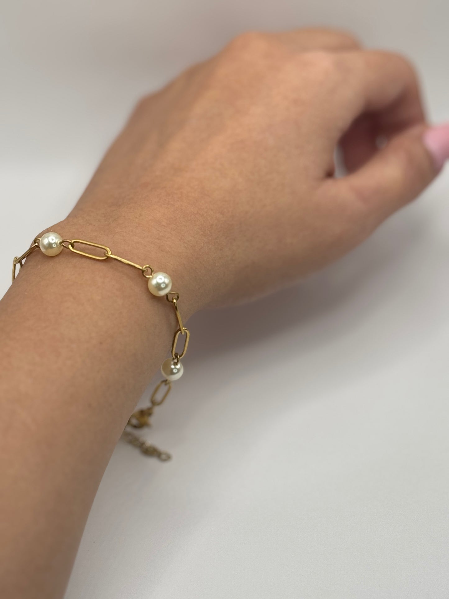 Gold paperclip chain bracelet with pearl accents worn on the wrist.