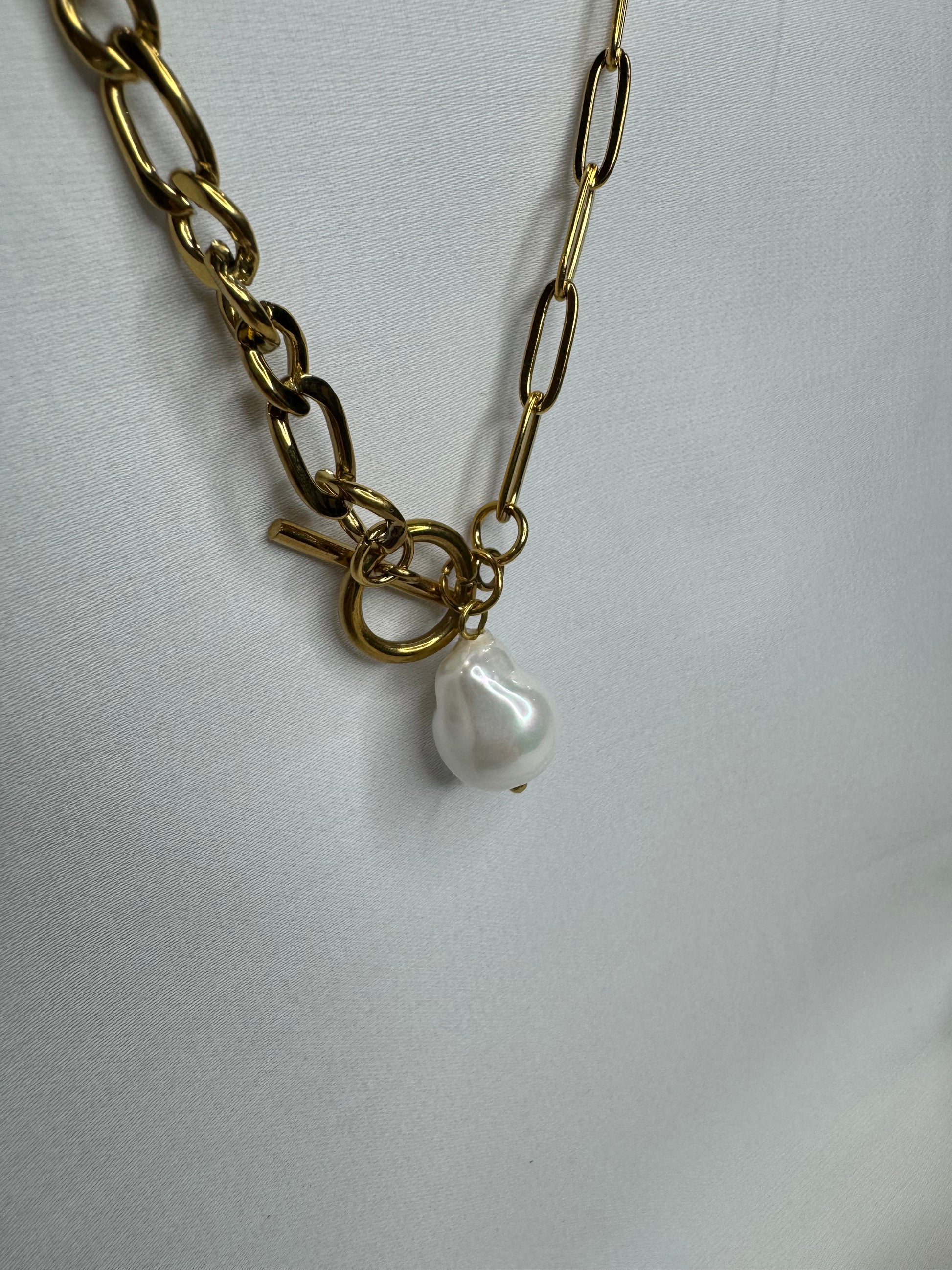 The Perla Necklace by EMPIECE™ — close-up of gold paperclip chain with toggle clasp and luminous pearl pendant on a soft white fabric background.
